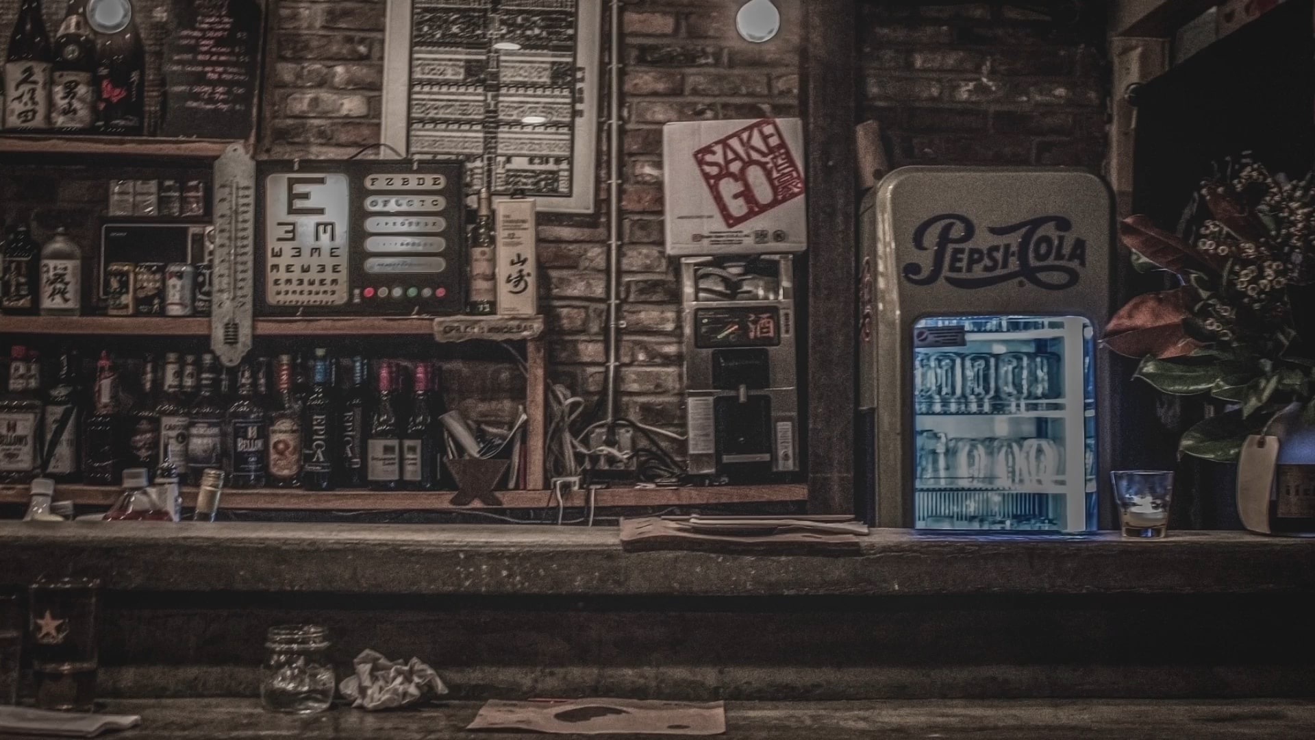 dimly lit bar with liquor bottles on shelves, a vintage Pepsi fridge, and a glass of whiskey on the counter