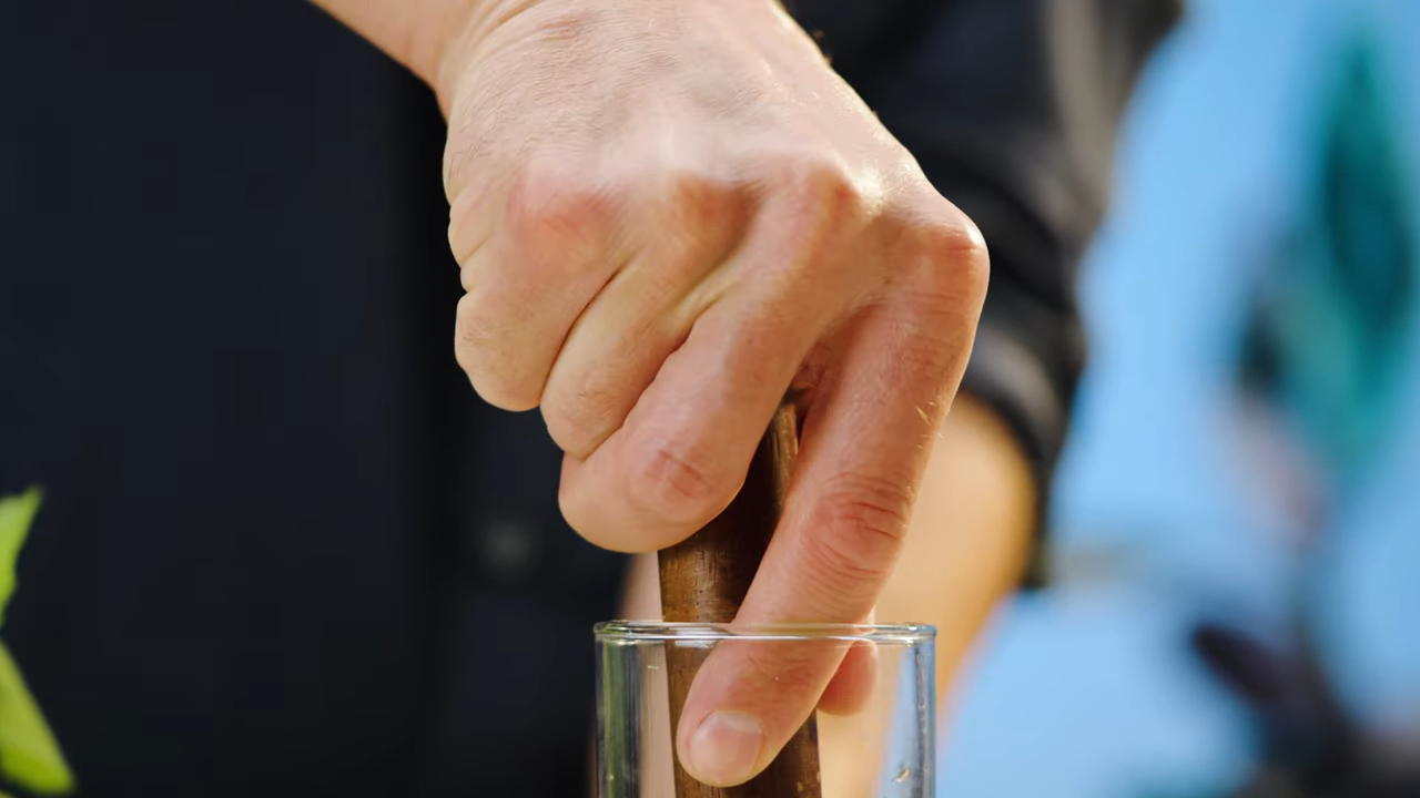 A hand using a wooden muddler to press ingredients in a clear glass