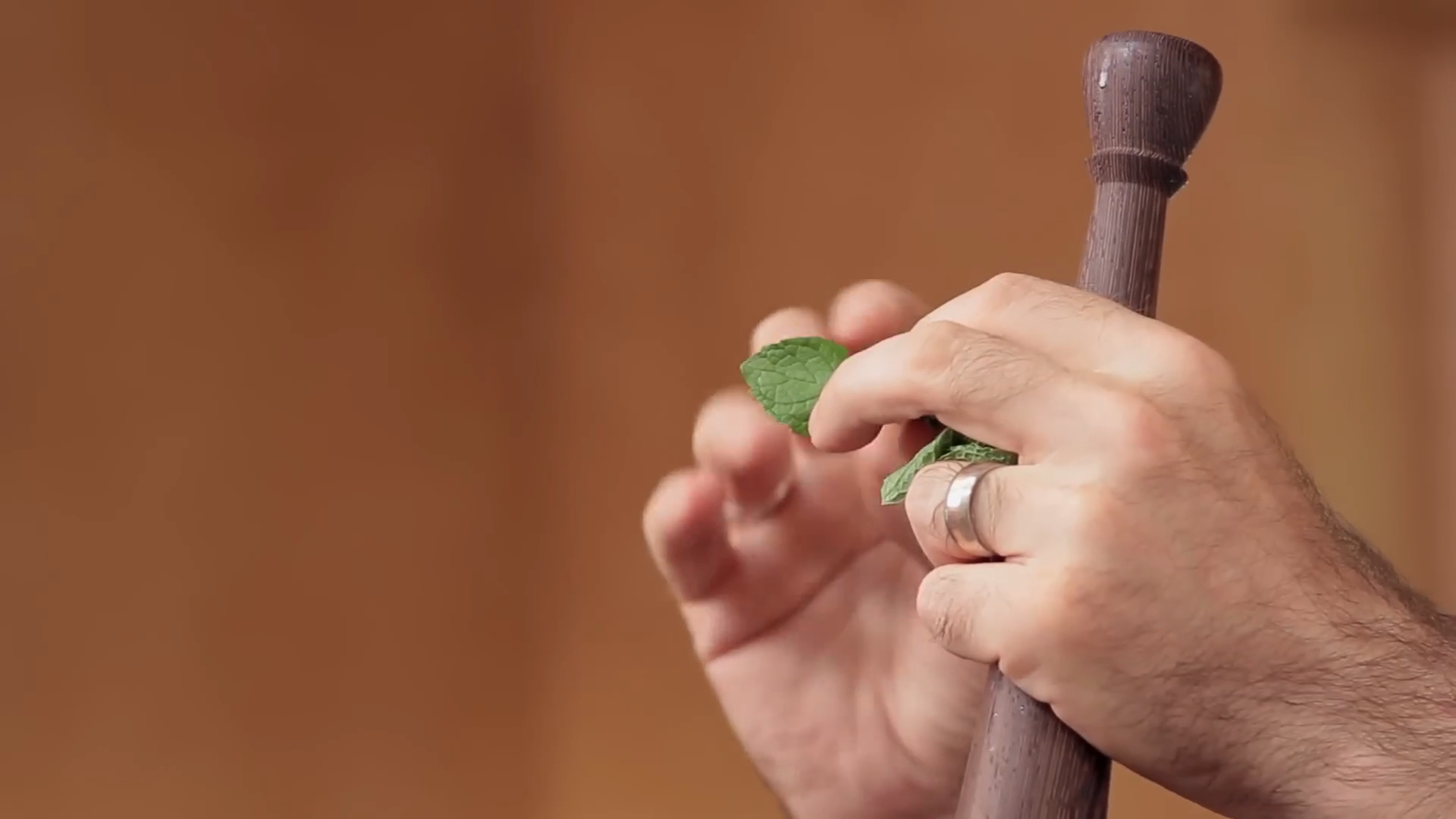 Close-up of hands holding fresh mint leaves and a wooden muddler, preparing ingredients