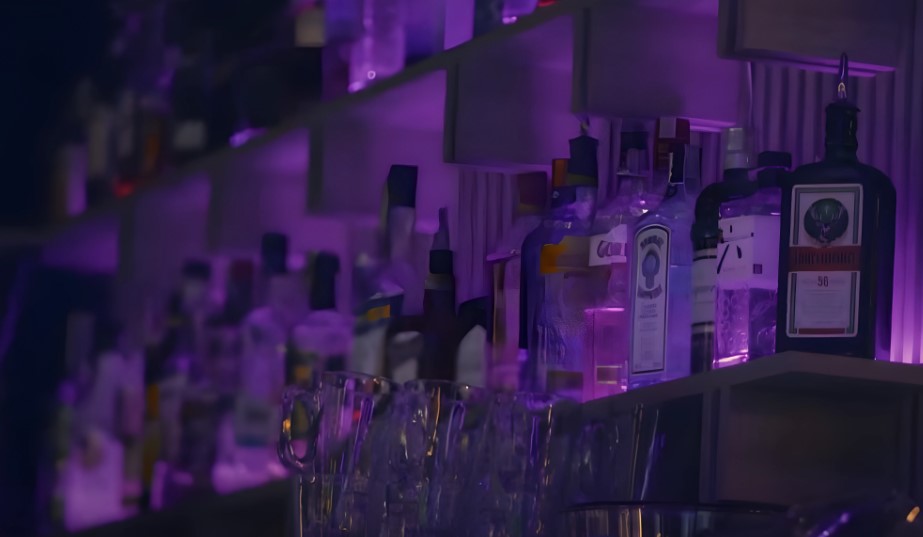 A well-stocked bar, showcasing a variety of liquors in purple-lit shelving