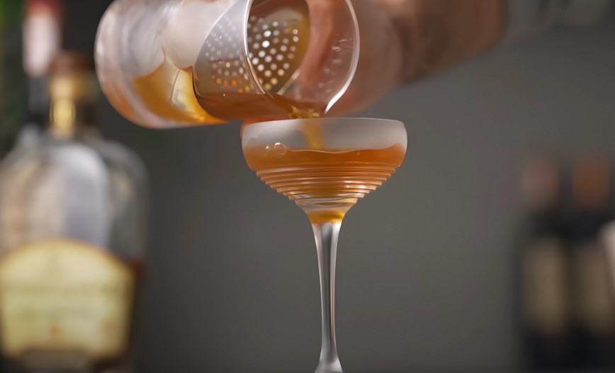 A cocktail is poured into a stemmed glass