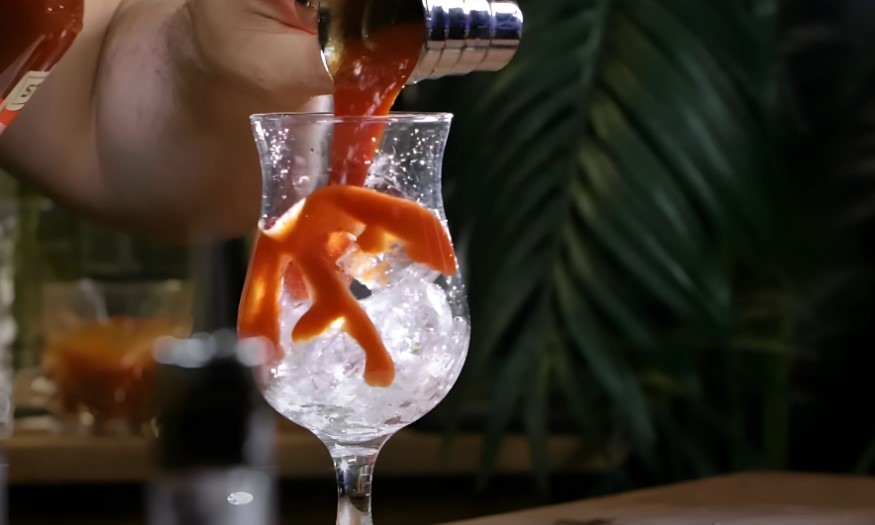 A bartender expertly pours a vibrant Bloody Mary into a chilled glass