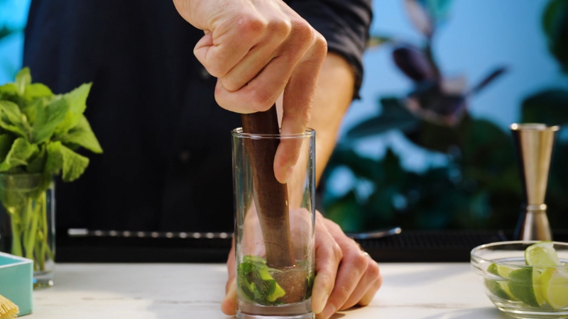 A Person Uses a Muddler to Crush Mint Leaves in A Glass for A Cocktail