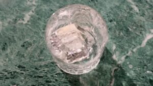 A Clear Glass with Large Ice Cubes Sits on A Green Marble Countertop