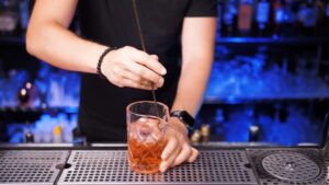 A Bartender Stirs a Negroni in A Mixing Glass with Ice at A Bar Counter