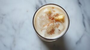 Top view of a creamy pineapple coconut cocktail in a glass, garnished with pineapple chunks and a sprinkle of cinnamon, served over ice on a marble background